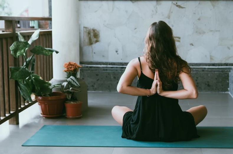 person sitting facing away with arms behind back in prayer pose