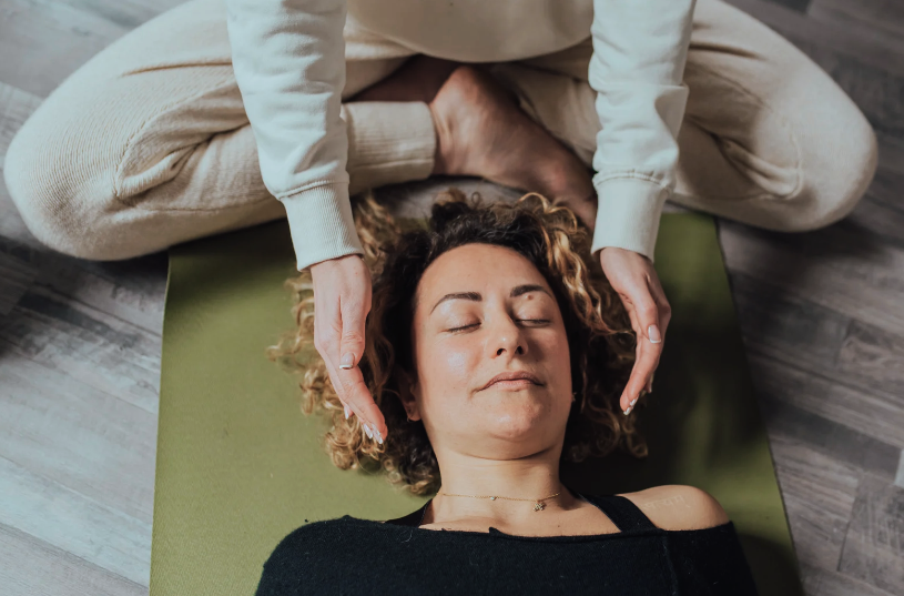 person laying down on yoga mat with another person's hands beside their head