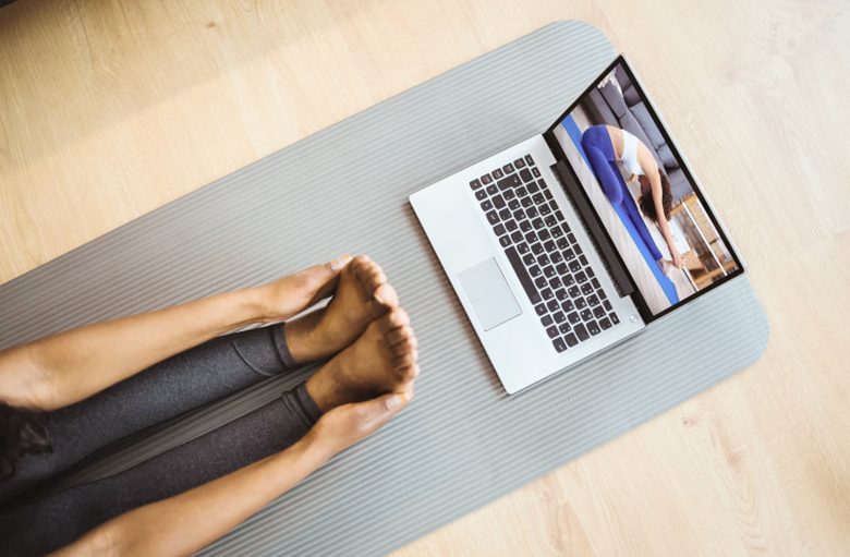 person's legs and arms shown facing a yoga video on a laptop